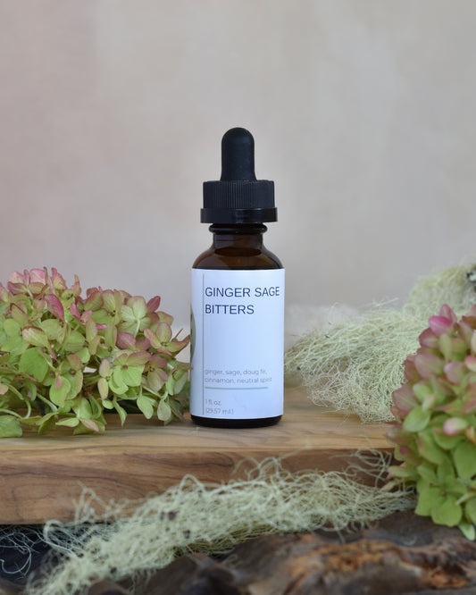 FreeWildShe Ginger Sage Bitters sit on a wooden tray. Lichen and hydrangea blooms surround the image.