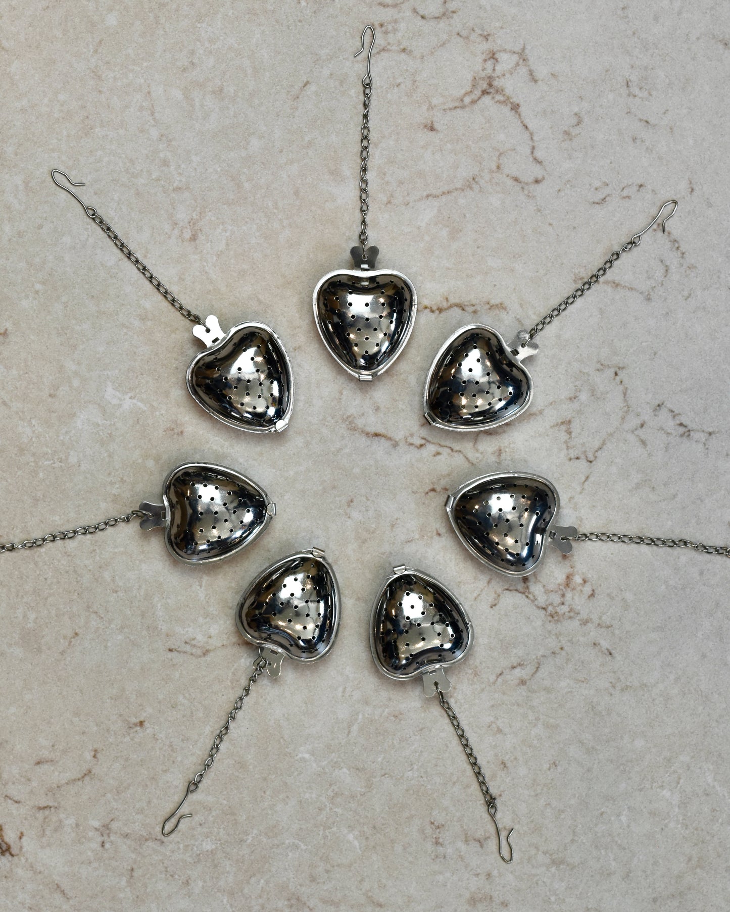 FreeWildShe Strawberry Infusers lined up in a wide circle with their chains pointing outward on a cream colored countertop.