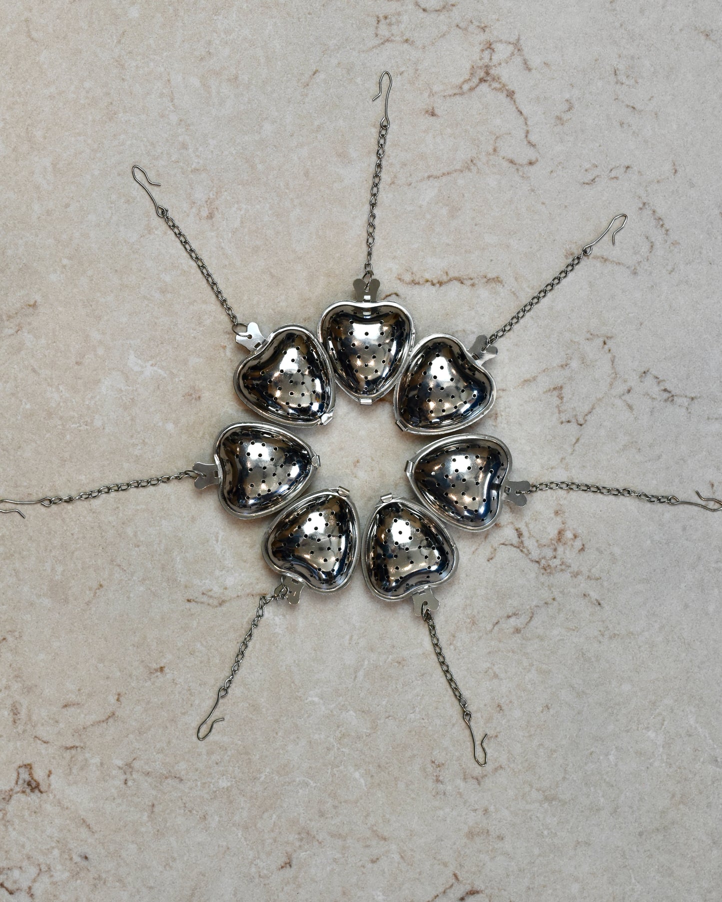 FreeWildShe Strawberry Infusers lined up in a circle with their chains pointing outward on a cream colored countertop.
