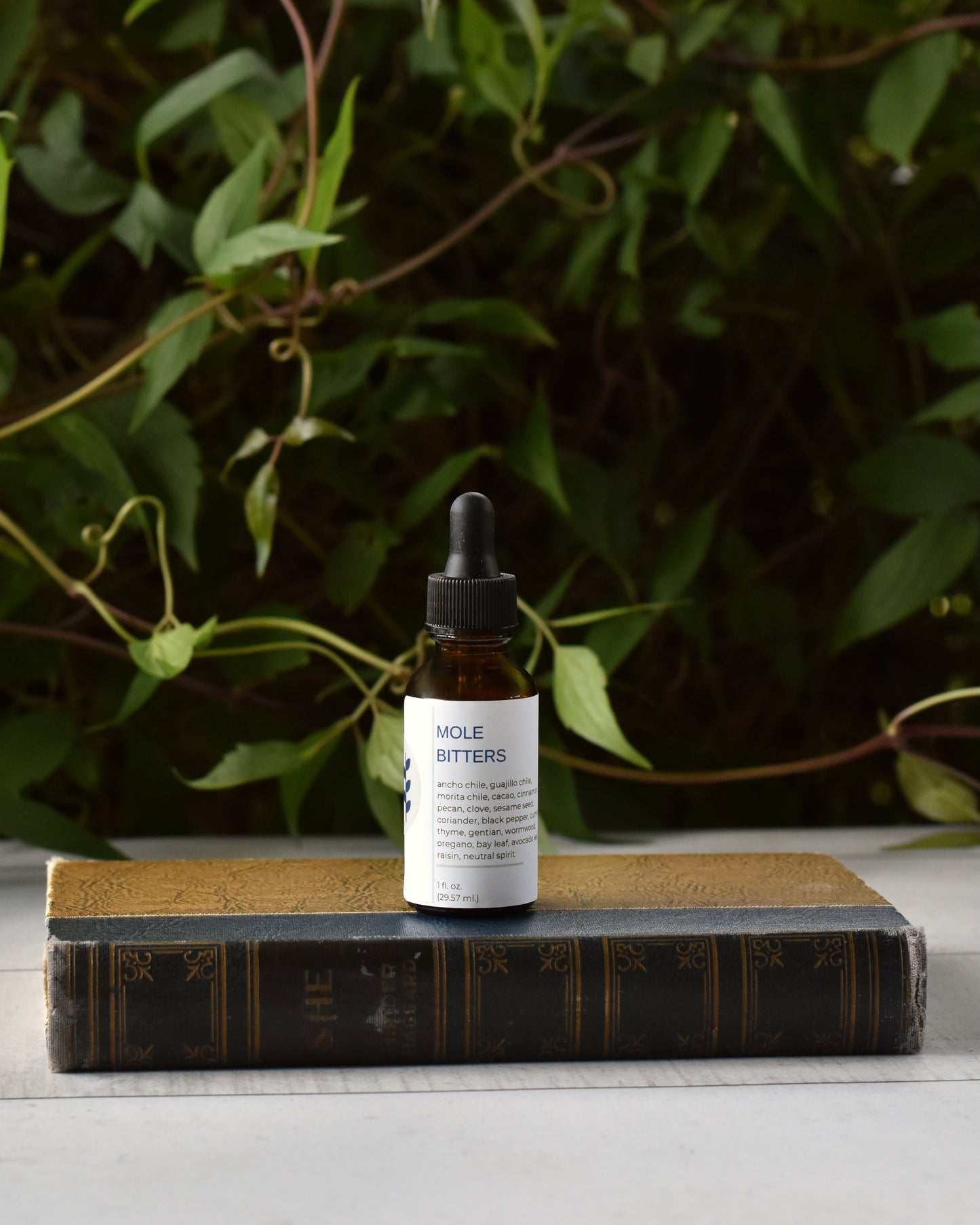 FreeWildShe Mole Bitters sit on an old book, in front of a green vine.