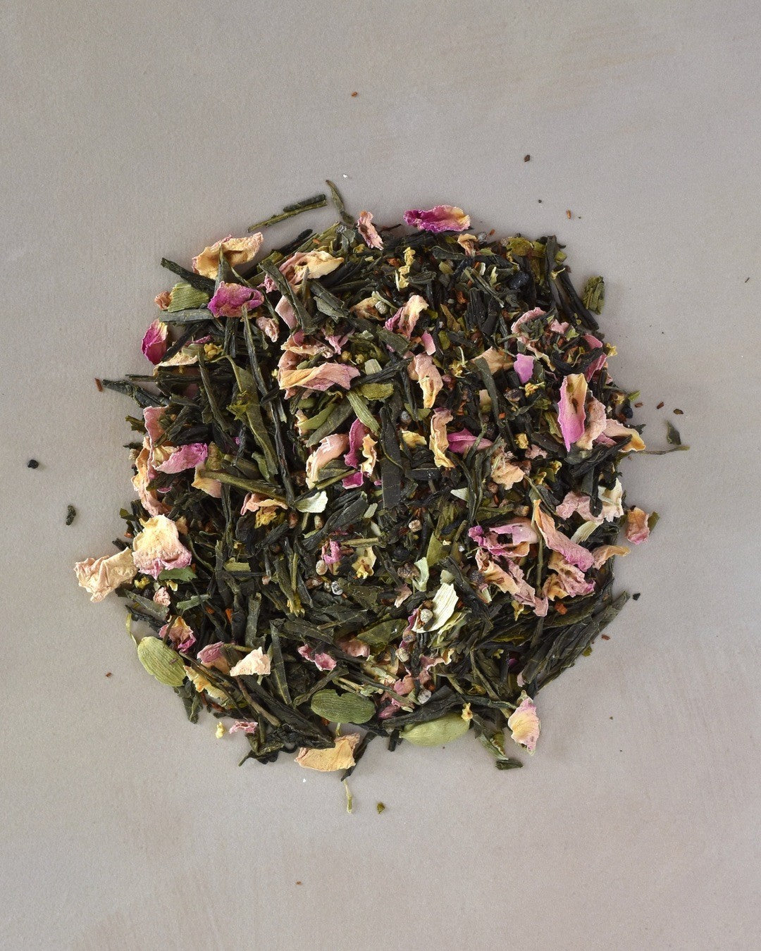 FreeWildShe Cardamom Rose Green Tea loose leaf ingredients lay in a pile on a cream countertop.