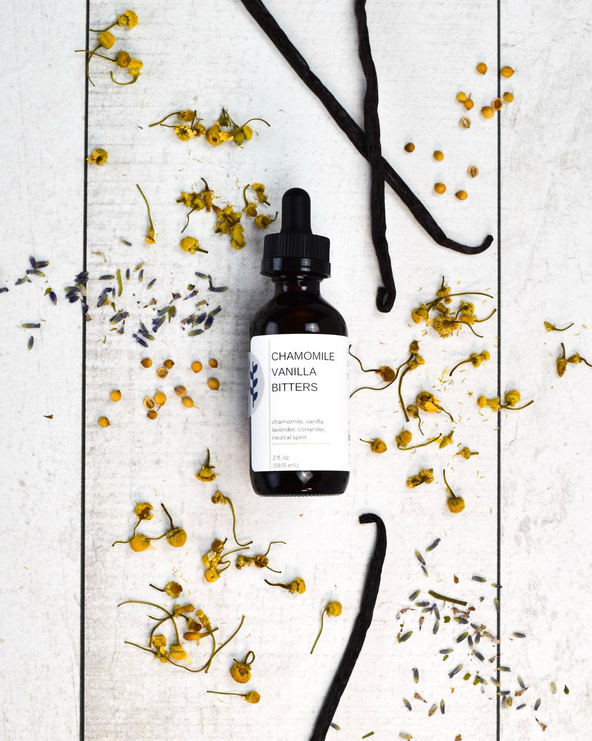 FreeWildShe Chamomile Vanilla Bitters on  white wooden table surrounded by botanicals.