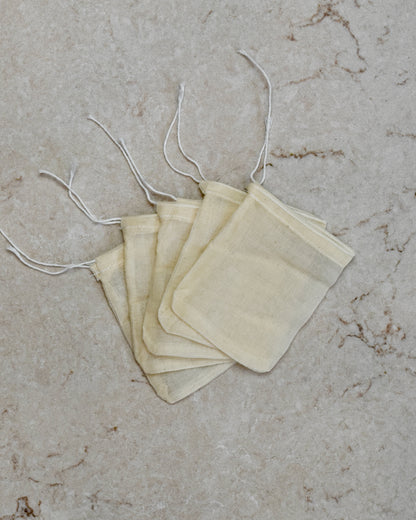 Five FreeWildShe Reusable Cotton Tea Bags lay spread out in the center on a cream colored countertop.