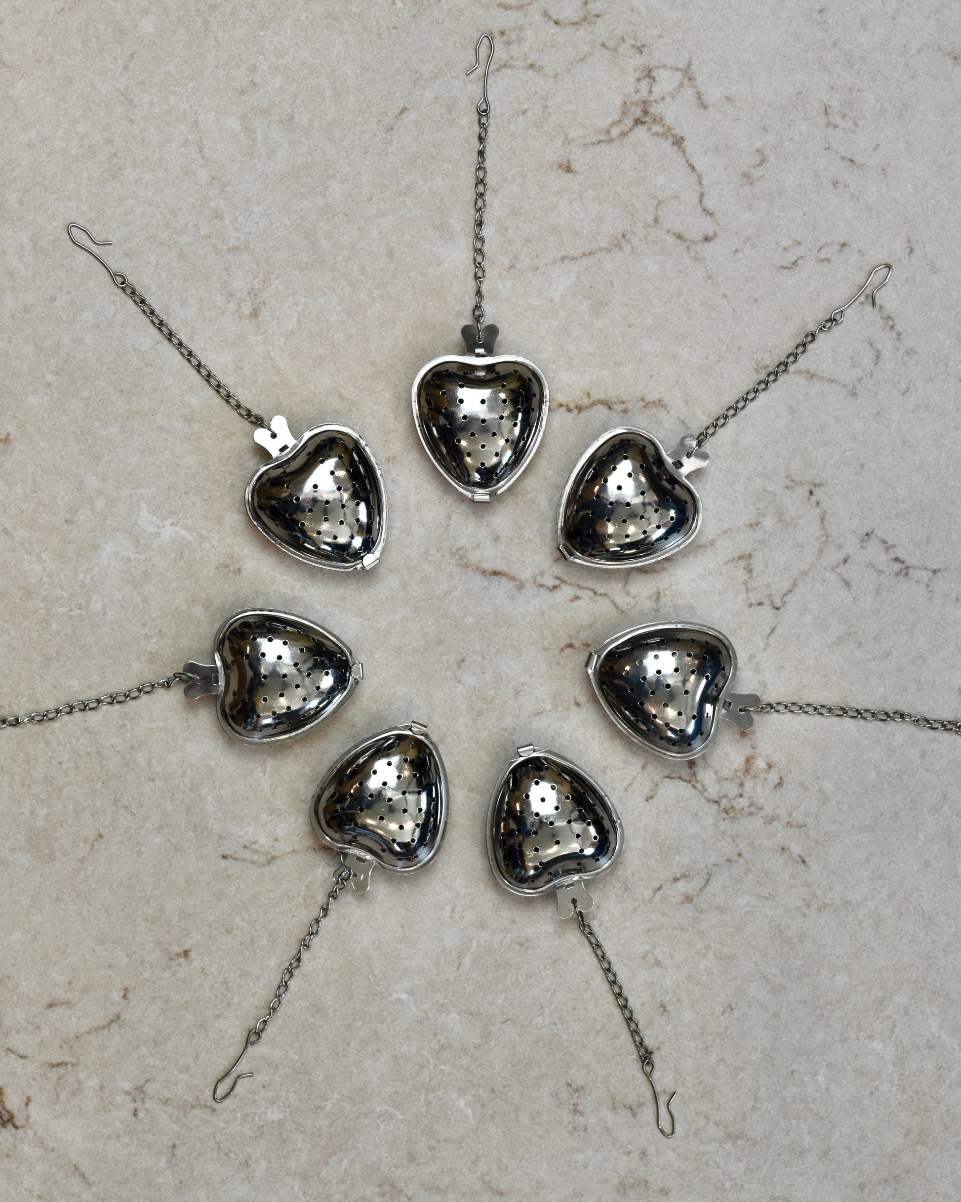 FreeWildShe Strawberry Infusers lined up in a wide circle with their chains pointing outward on a cream colored countertop.