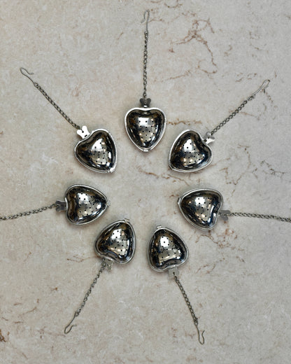FreeWildShe Strawberry Infusers lined up in a wide circle with their chains pointing outward on a cream colored countertop.