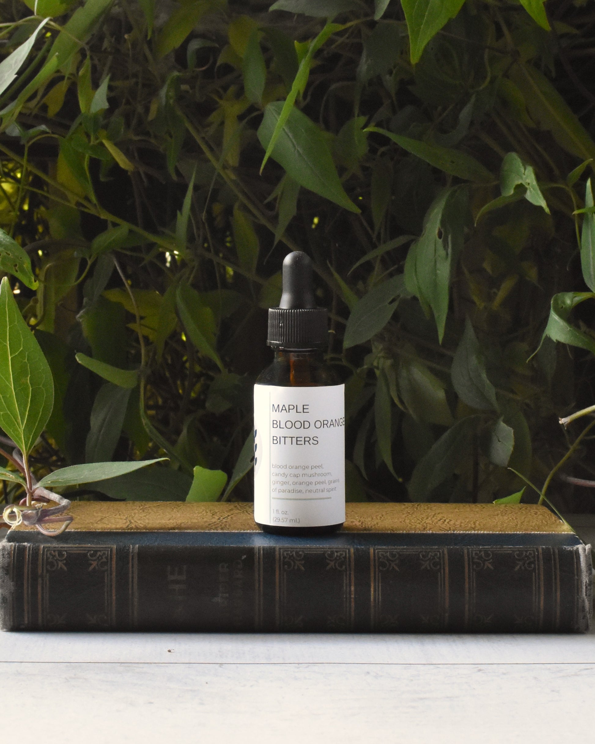 FreeWildShe Maple Blood Orange Bitters sit on an old book, in front of a green vine.