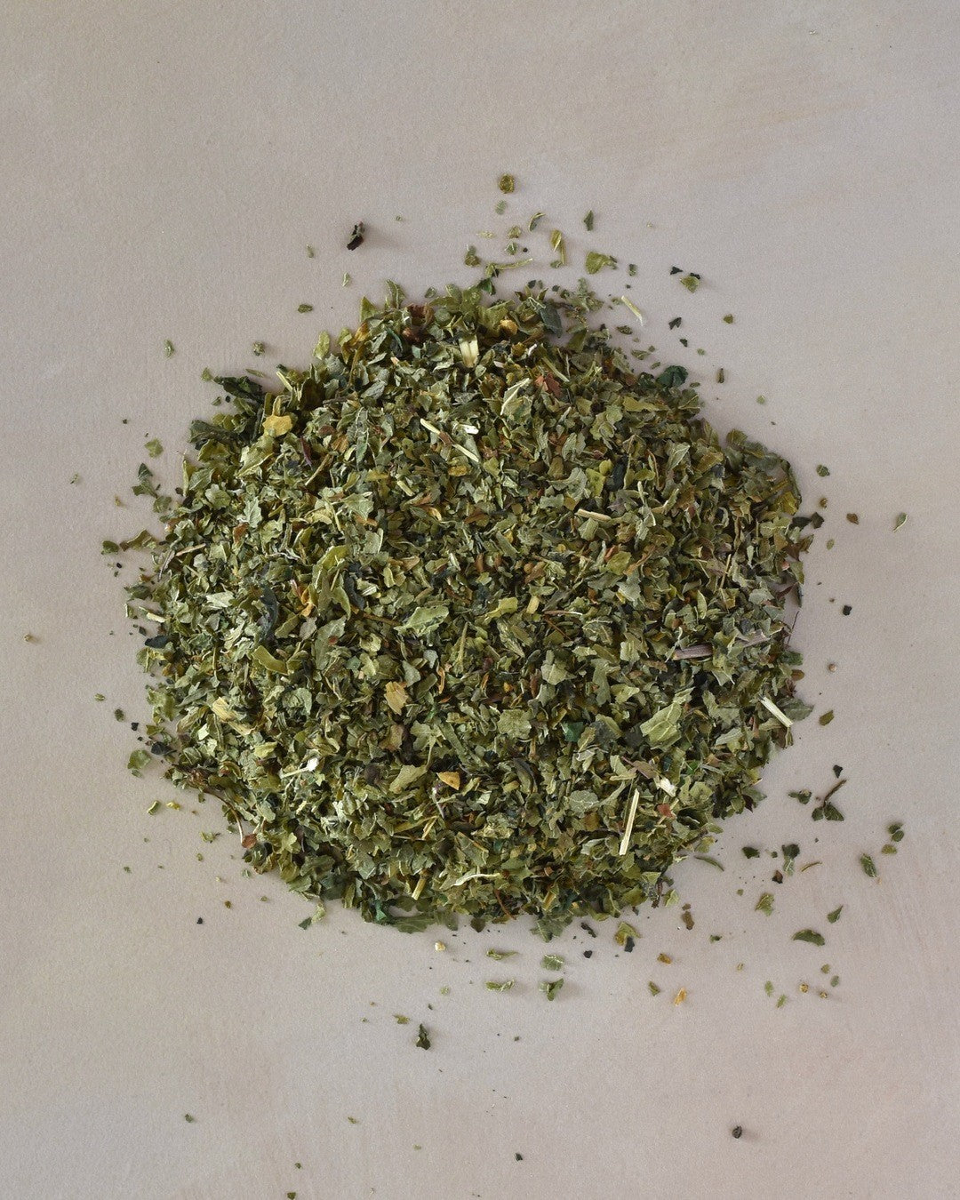 FreeWildShe Nettle Herbal Tea loose leaf ingredients lay in a pile on a cream countertop.