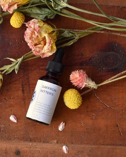 FreeWildShe Saffron Bitters lay on a box surrounded by dried botanicals.