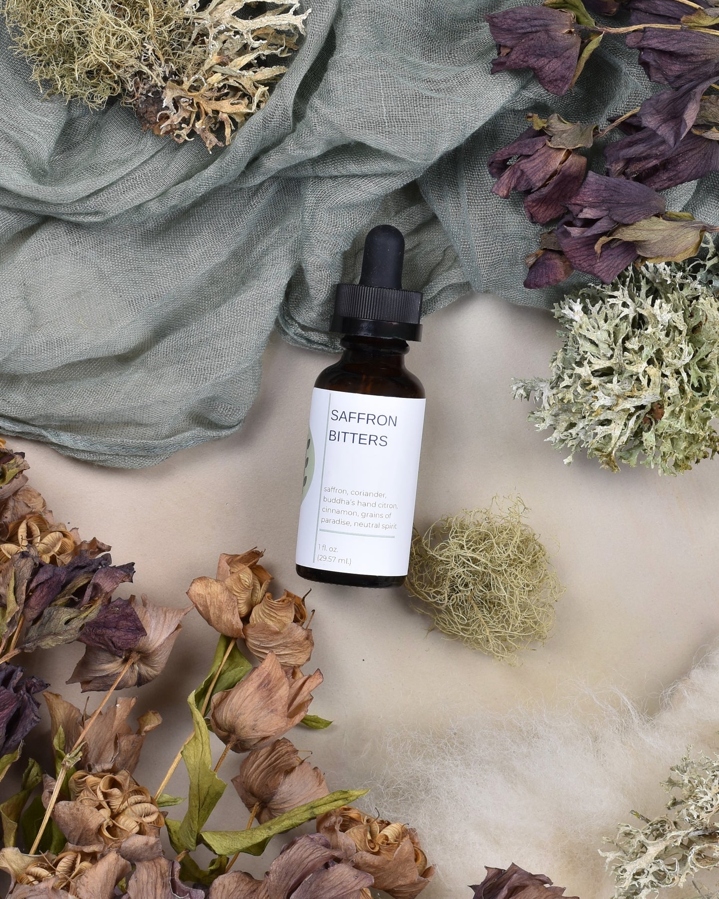 FreeWildShe Saffron Bitters lay on green fabric surrounded by dried flowers and lichen.