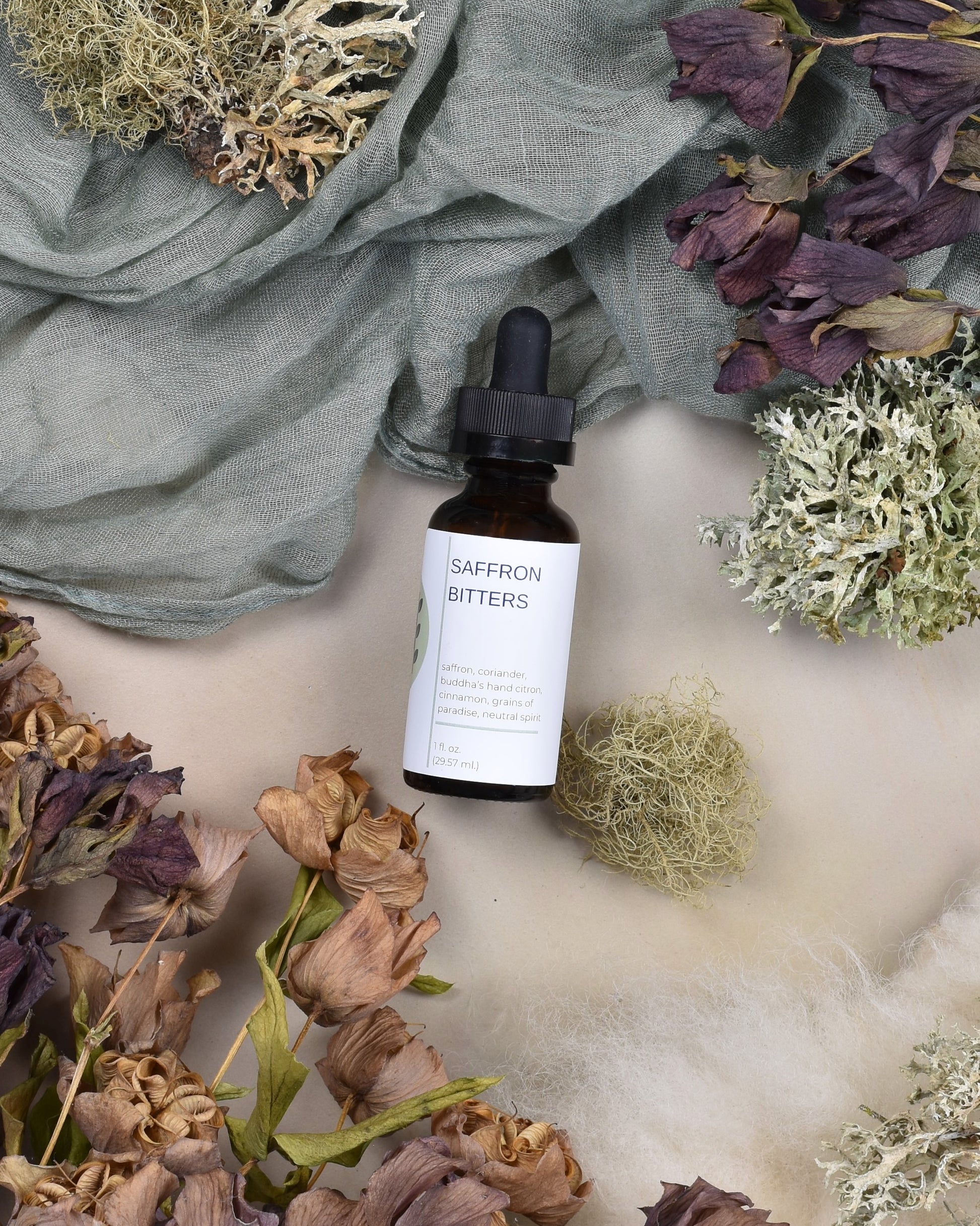 FreeWildShe Saffron Bitters lay on green fabric surrounded by dried flowers and lichen.