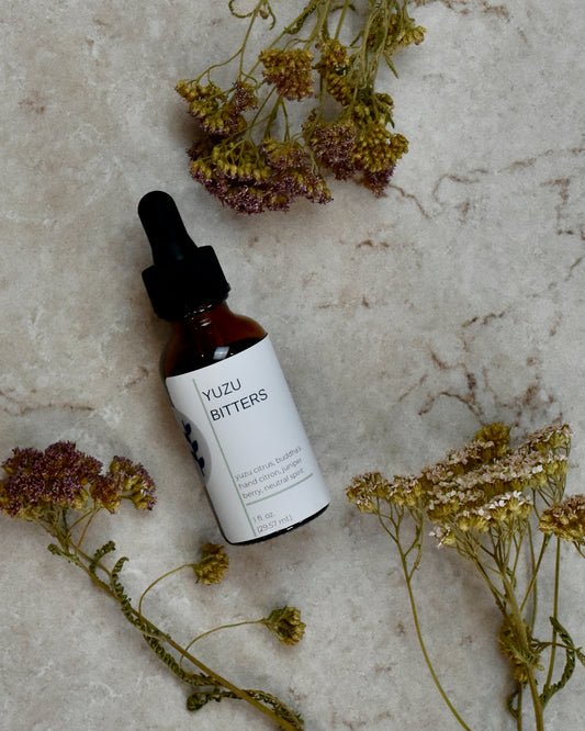FreeWildShe Yuzu Bitters lay on a cream colored countertop. Dried flowers are scattered around.